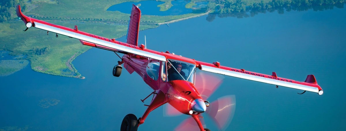 Red Draco aircraft in flight over blue water with the pilot visible in the cockpit